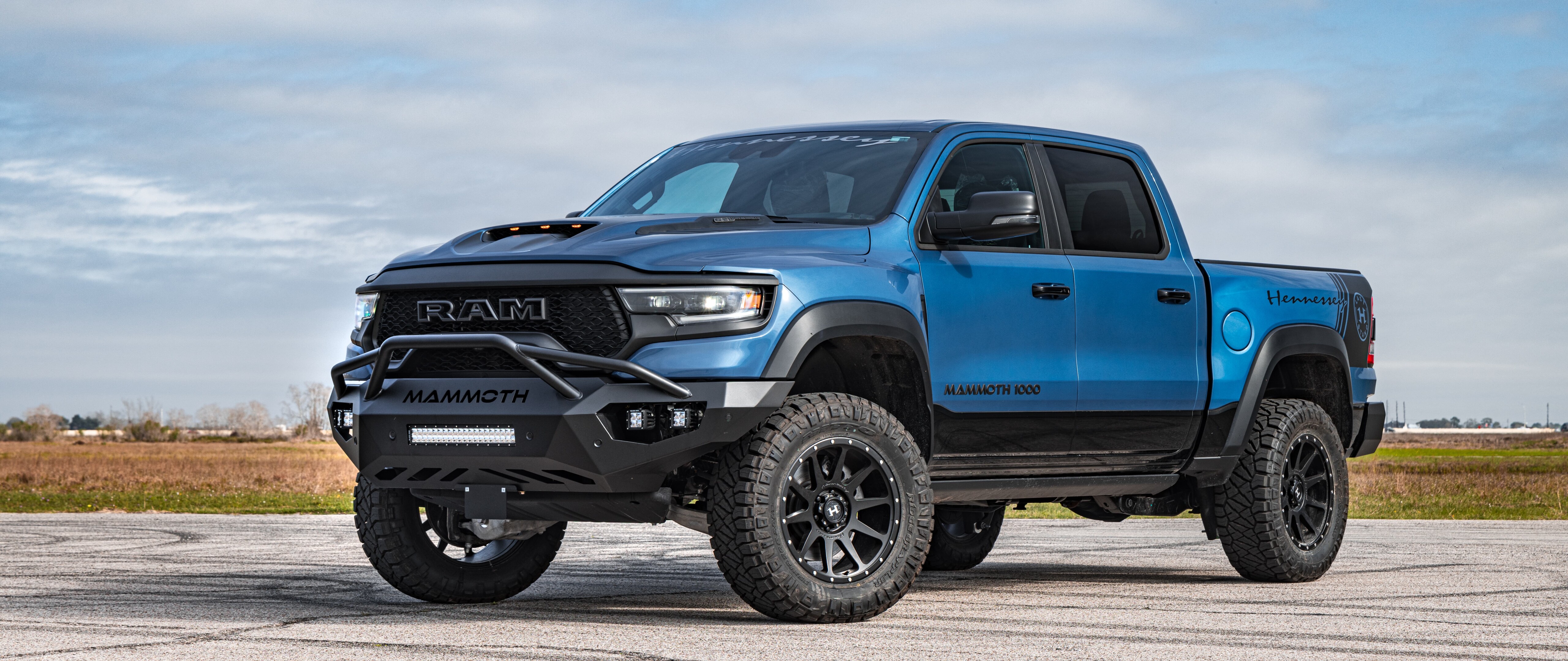 Uma imponente caminhonete Hennessey Mammoth 1000 Dodge Ram, com suspensão elevada, modificações robustas para uso off-road e carroceria alargada.