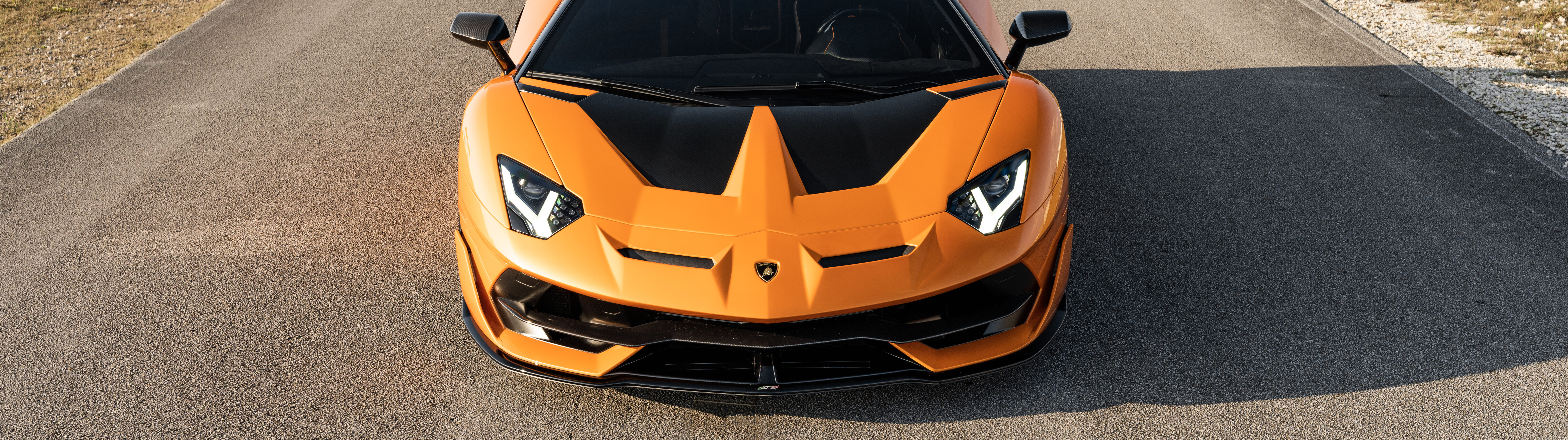 Uma imagem em close-up de um Lamborghini Aventador SVJ, destacando a sua elegante carroçaria aerodinâmica e a imponente silhueta de supercarro.